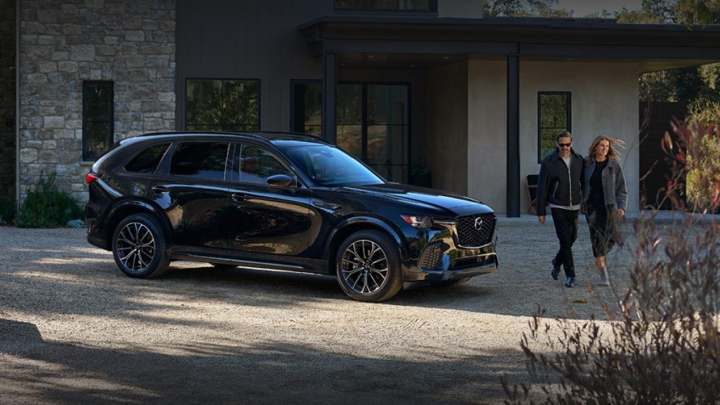 A couple walking beside a black Mazda SUV in front of a house.